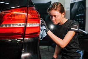 Final polishing. Modern black automobile get cleaned by woman inside of car wash station photo