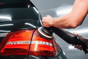 Guy polishing surface of vehicle. Modern black automobile get cleaned by man inside of car wash station photo