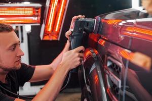 Guy polishing surface of vehicle. Modern black automobile get cleaned by man inside of car wash station photo