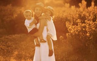 Happy family of mother, little son and daughter spending free time on the field at sunny day time of summer photo
