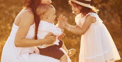 Happy family of mother, little son and daughter spending free time on the field at sunny day time of summer photo