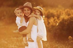 Happy family of mother, little son and daughter spending free time on the field at sunny day time of summer photo