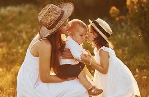 Happy family of mother, little son and daughter spending free time on the field at sunny day time of summer photo