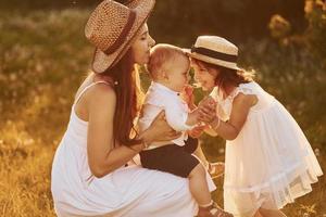 Happy family of mother, little son and daughter spending free time on the field at sunny day time of summer photo