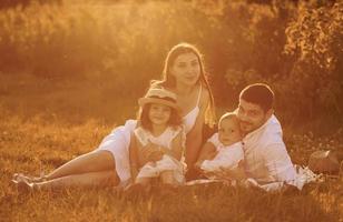 Sitting on the grass. Father, mother with daughter and son spending free time outdoors at sunny day time of summer photo