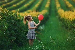 una niña positiva con un globo rojo en las manos se divierte en el campo durante el día de verano foto