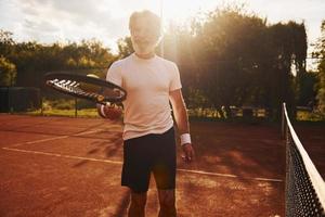 tiempo de entrenamiento. Senior hombre moderno y elegante con raqueta al aire libre en la cancha de tenis durante el día