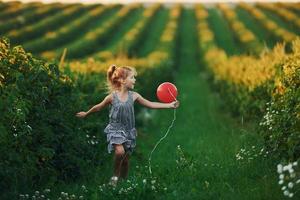 Positive little girl with red balloon in hands have fun on the field at summer day time photo