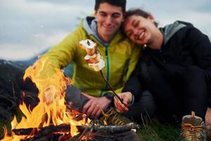 Couple with marshmallow near campfire. Majestic Carpathian Mountains. Beautiful landscape of untouched nature photo