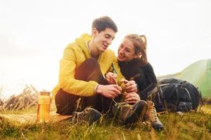 Young lovely couple sitting near tent outdoors at daytime. Beautiful sunlight photo