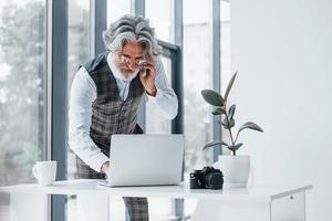 Boss in formal clothes works in office. Senior stylish modern man with grey hair and beard indoors photo