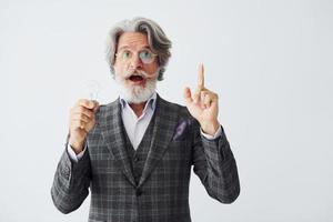 con bombilla en las manos. Senior hombre moderno con estilo con pelo gris y barba en el interior foto