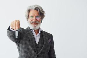 Holds car keys in hand. Senior stylish modern man with grey hair and beard indoors photo