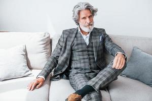 In apartment with elegant clothes. Senior stylish modern man with grey hair and beard indoors photo