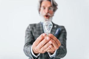 With light bulb in hands. Senior stylish modern man with grey hair and beard indoors photo