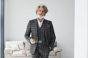 In apartment with elegant clothes. Senior stylish modern man with grey hair and beard indoors photo