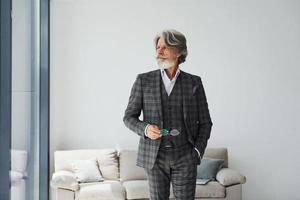 en apartamento con ropa elegante. Senior hombre moderno con estilo con pelo gris y barba en el interior foto