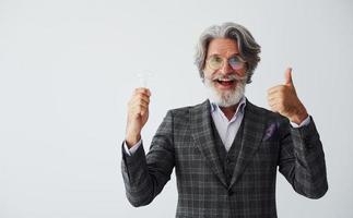 con bombilla en las manos. Senior hombre moderno con estilo con pelo gris y barba en el interior foto