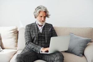 In apartment with elegant clothes. Senior stylish modern man with grey hair and beard indoors photo