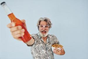 Bottle of drink and popcorn in hands. Senior stylish modern man with grey hair and beard indoors photo