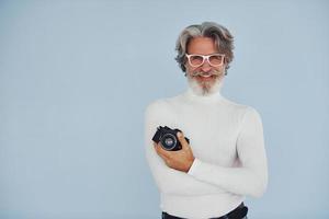 fotógrafo con cámara vintage. Senior hombre moderno con estilo con pelo gris y barba en el interior foto