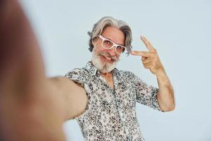turista hace selfie. Senior hombre moderno con estilo con pelo gris y barba en el interior foto