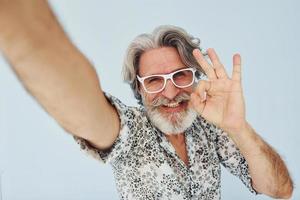 Tourist makes selfie. Senior stylish modern man with grey hair and beard indoors photo