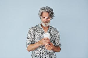 Cup of drink in hands. Senior stylish modern man with grey hair and beard indoors photo
