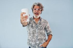 taza de bebida en las manos. Senior hombre moderno con estilo con pelo gris y barba en el interior foto