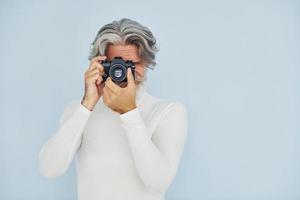 fotógrafo con cámara vintage. Senior hombre moderno con estilo con pelo gris y barba en el interior foto