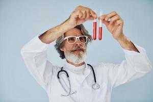 Doctor holds test tubes. Senior stylish modern man with grey hair and beard indoors photo