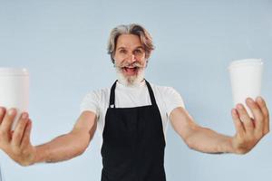 camarero con bebidas en las manos. Senior hombre moderno con estilo con pelo gris y barba en el interior foto