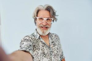 Tourist makes selfie. Senior stylish modern man with grey hair and beard indoors photo