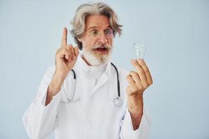 Medical worker holds light bulb in hands. Senior stylish modern man with grey hair and beard indoors photo