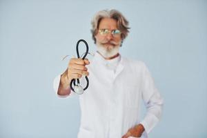 doctor en bata blanca contra la pared. Senior hombre moderno con estilo con pelo gris y barba en el interior foto