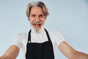 camarero alegre toma selfie. Senior hombre moderno con estilo con pelo gris y barba en el interior foto