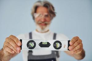 Worker in uniform holds level matching device. Senior stylish modern man with grey hair and beard indoors photo