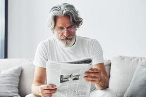 descansando en el sofá. Senior hombre moderno con estilo con pelo gris y barba en el interior foto