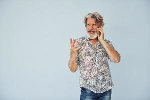 Having call when standing against wall. Senior stylish modern man with grey hair and beard indoors photo