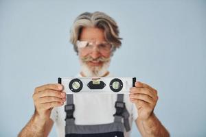 el trabajador en uniforme tiene un dispositivo de coincidencia de nivel. Senior hombre moderno con estilo con pelo gris y barba en el interior foto