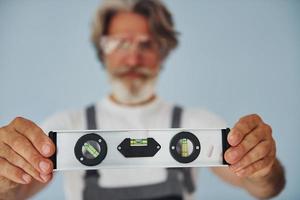 Worker in uniform holds level matching device. Senior stylish modern man with grey hair and beard indoors photo