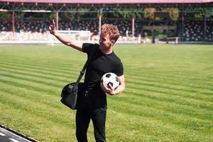 Football player on the field. Sportive young guy in black shirt and pants outdoors at daytime photo