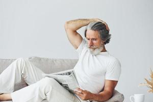 descansando en el sofá. Senior hombre moderno con estilo con pelo gris y barba en el interior foto