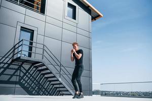 Warming up near black building. Sportive young guy in black shirt and pants outdoors photo