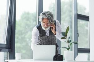 Successful businessman uses phone. Senior stylish modern man with grey hair and beard indoors photo