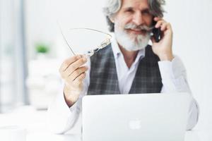 Successful businessman uses phone. Senior stylish modern man with grey hair and beard indoors photo