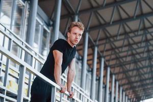 Taking a break. Sportive young guy in black shirt and pants outdoors at daytime photo