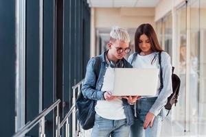 Two young student friends together in a corridor of a college with laptop in hands photo