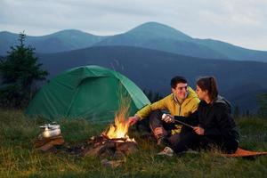 Classical marshmallow making near campfire. Young couple. Majestic Carpathian Mountains. Beautiful landscape of untouched nature photo