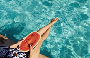 Young woman sits near swimming pool at daytime with watermelon photo